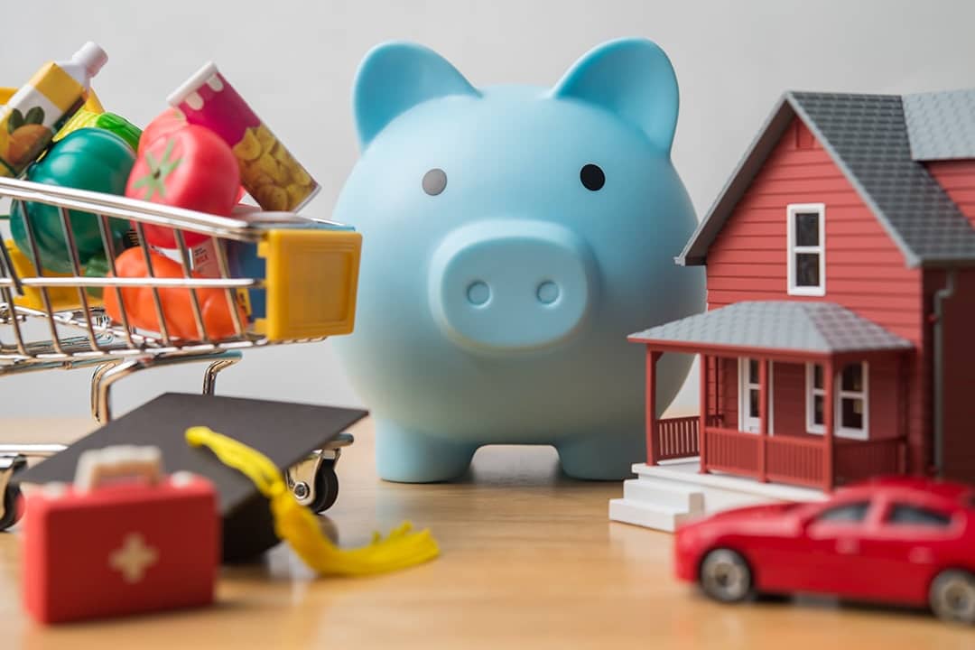 Physical figures of expense concepts such as mortgage, car, groceries around a piggy bank as a concept of budgeting and saving.